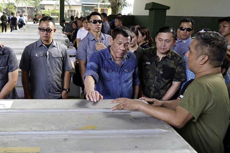 Filipinernas president  Rodrigo Duterte (mitten med blå skjorta) vid en av kistorna med kvarlevorna efter ett av offren för söndagens bombdåd. Myndigheterna säger att de kommer att ”jaga de här hänsynslösa förövarna till världens ände”, enligt AP.