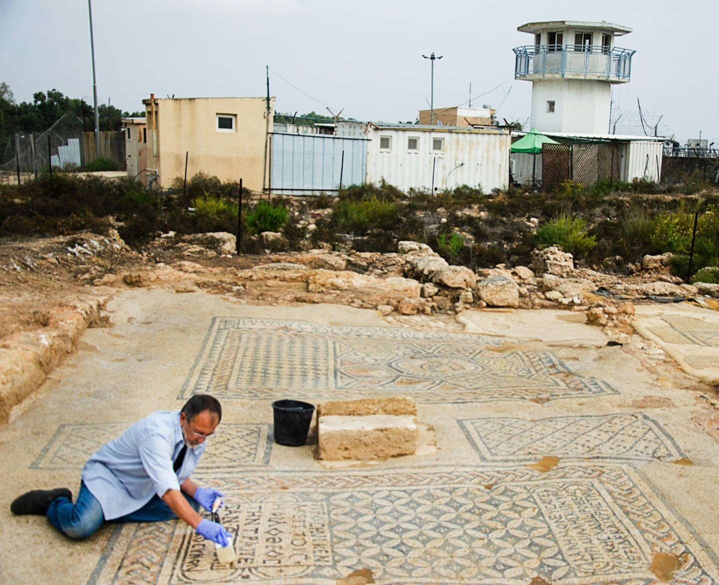 En israelisk arkeolog frilägger mosaiken i Megiddo med platsens fängelse i bakgrunden.