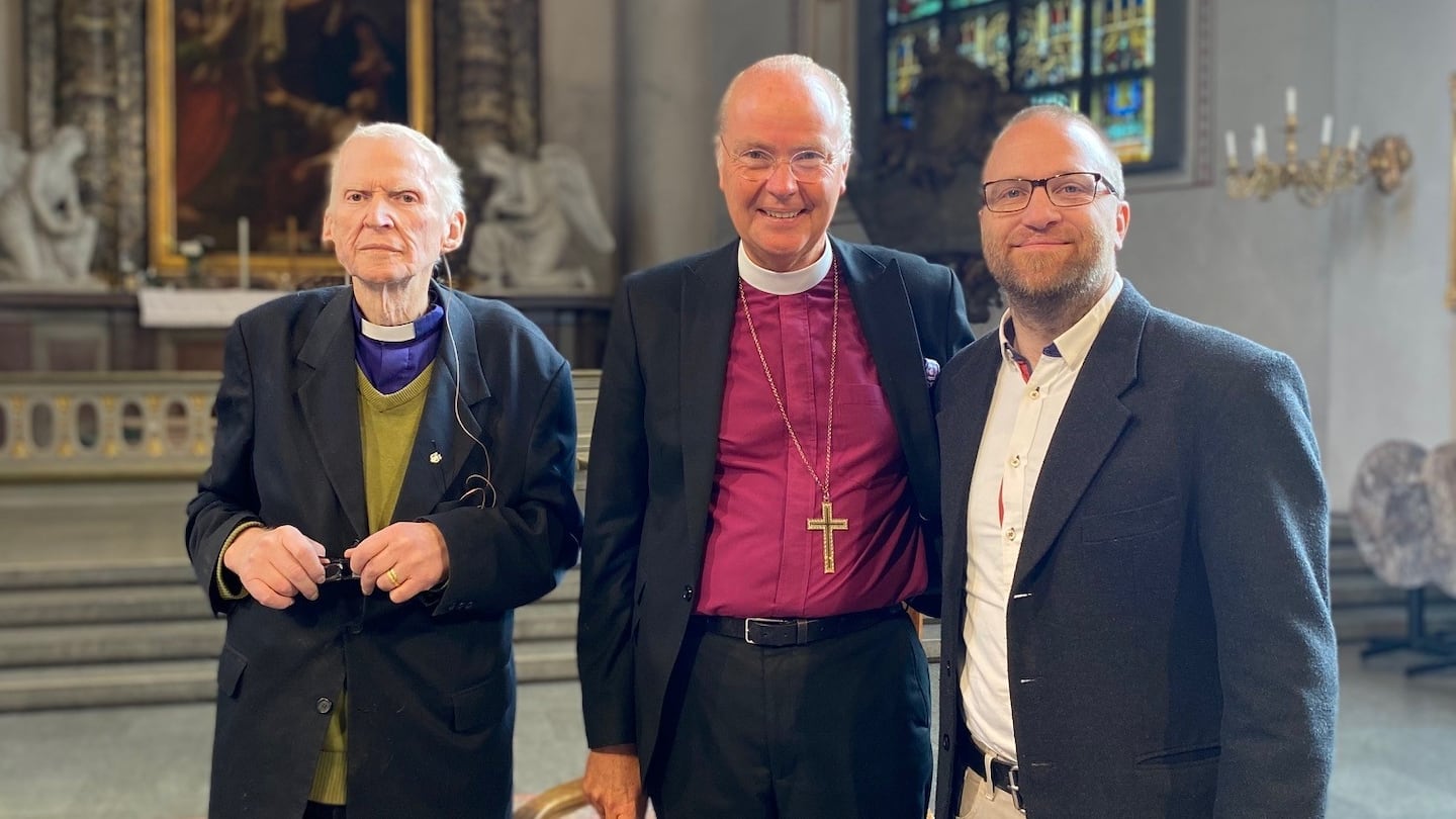 Tre personer står i en kyrka och ser glada ut.