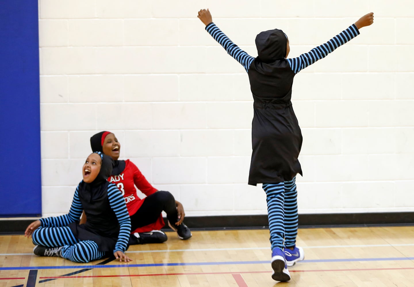 Tre flickor i hijab jublar i en sporthall.