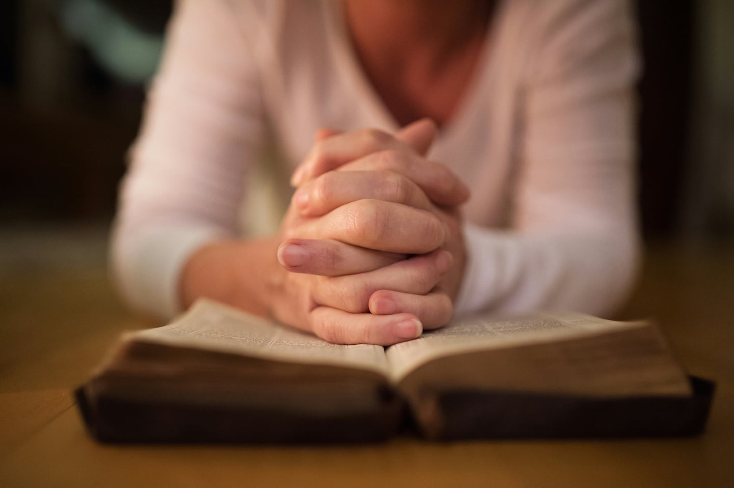 En kvinna i vit tröja vilar sina knäppta händer mot en uppslagen stor bibel,