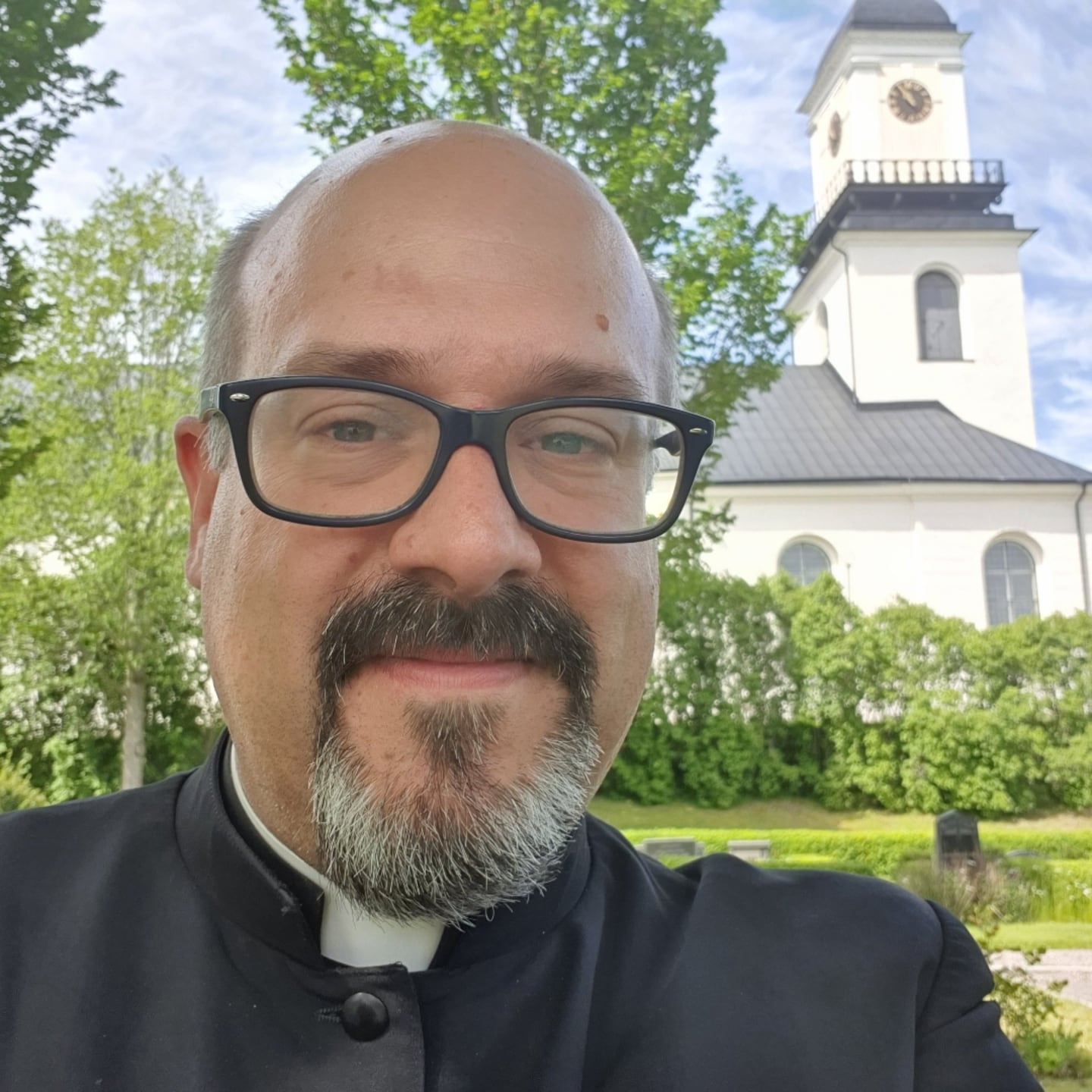 En man i prästkrage med en kyrka i bakgrunden.